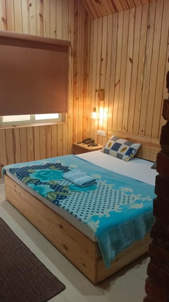 Double bed with bedside lamp in a warm wood-paneled cottage.